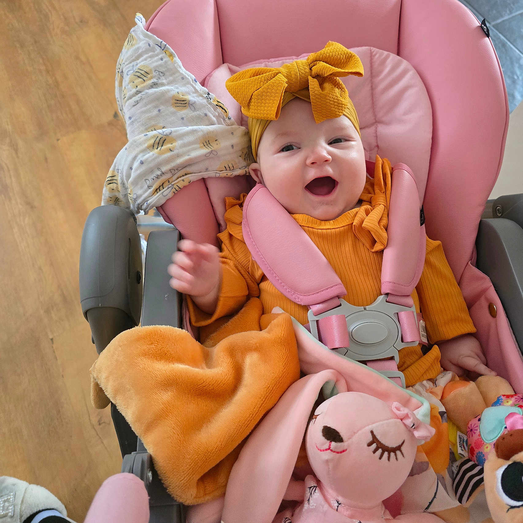 Eva-Willow is registered to the contest to win money with this photo: baby, blanket, bow, child, clothing, comfort, cute, happy, headband, indoor, infant, person, pink, plush_toy, seat_belt, smiling, stroller, toy, wood_floor, yellow