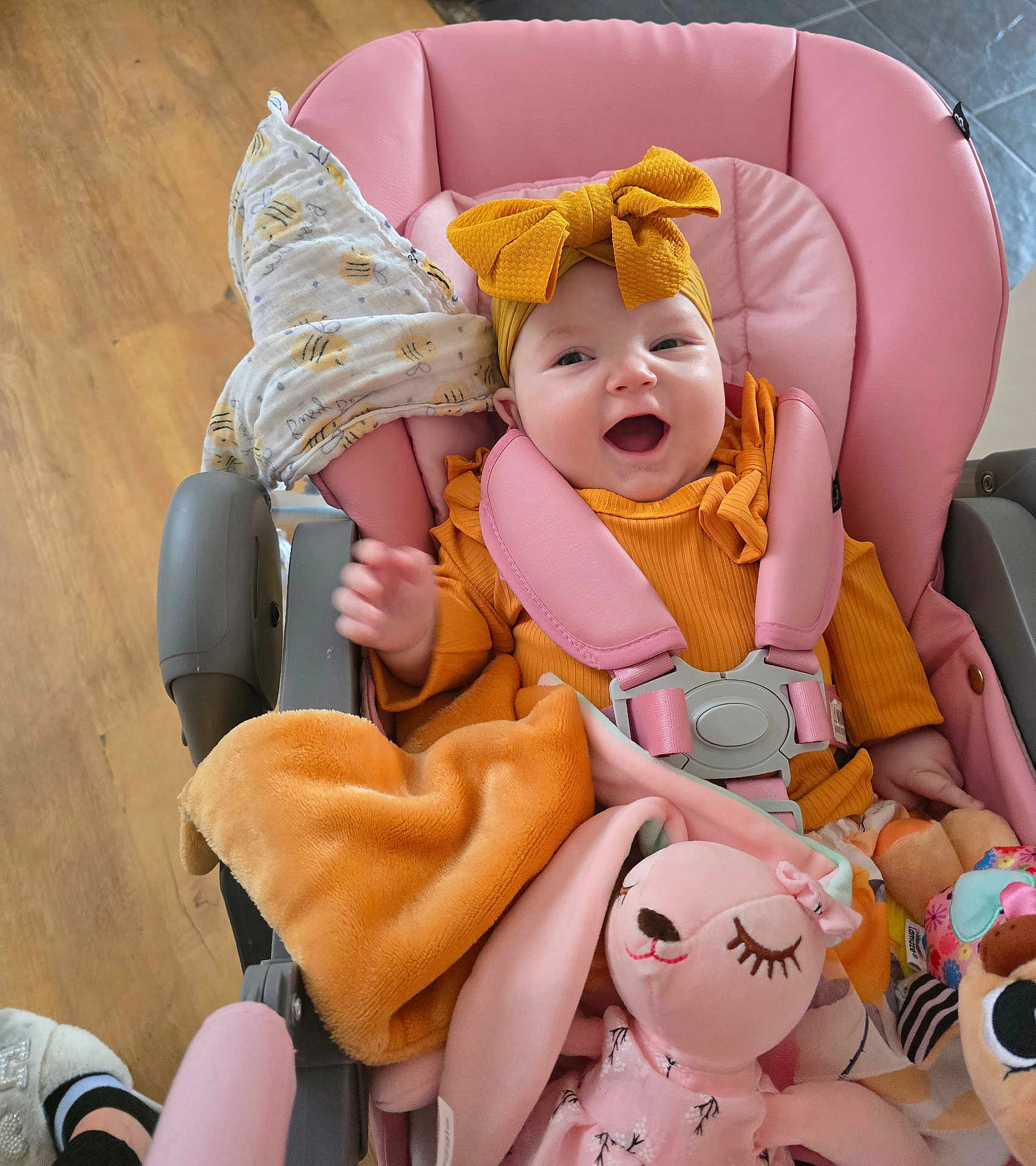 Eva-Willow is registered to the contest to win money with this photo: baby, child, smiling, stroller, pink, yellow, headband, bow, blanket, plush_toy, toy, happy, indoor, clothing, seat_belt, wood_floor, person, cute, infant, comfort