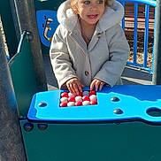 Irina a rejoint le concours — aidez-le/la à gagner de superbes lots ! bench, blue_panel, candid, child, coat, face, hands, hood, jacket, outdoor, park, play_equipment, playground, railing, smile, sunlit, toddler, toy, trees, woodchips