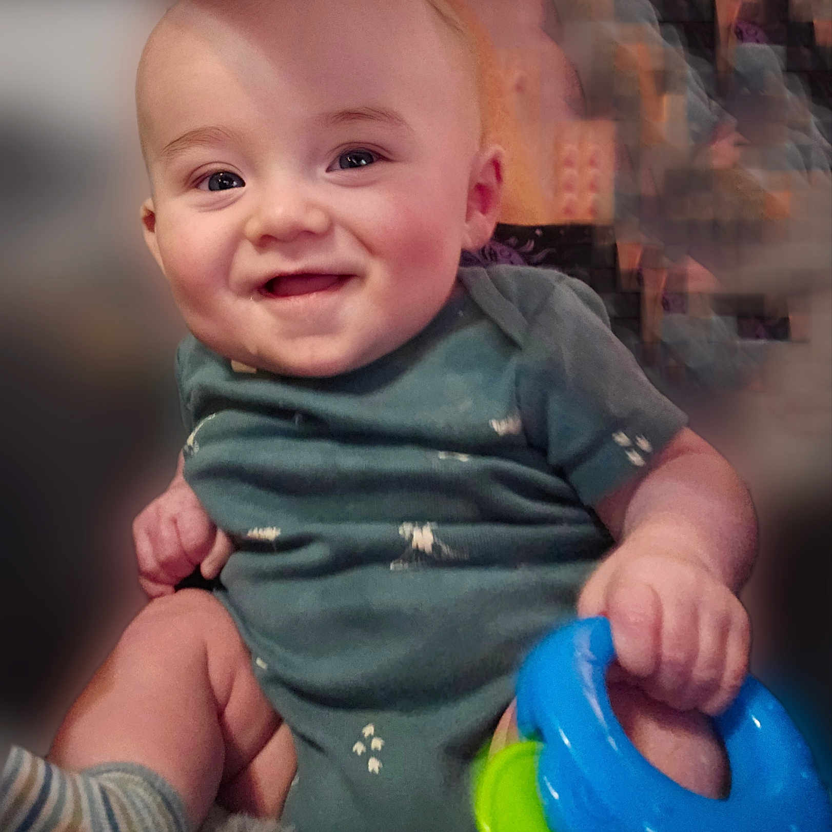 Dimitri joined the competition — help win amazing prizes! baby, smiling, child, toy, colorful, hand, face, blue, green, clothing, short_sleeve, sitting, cute, infant, happy, indoors, skin, portrait, play, young