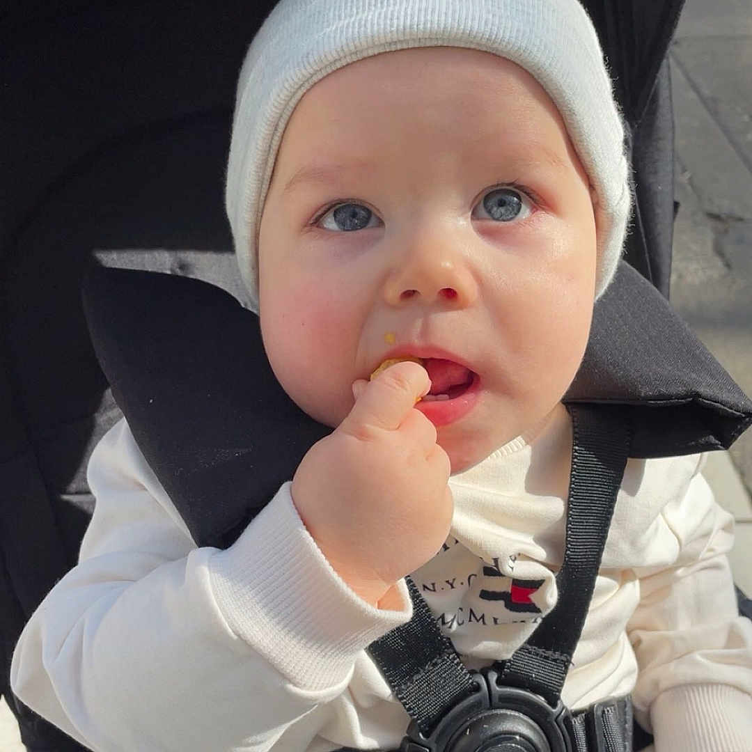 Mael participe au concours pour gagner de l'argent avec cette photo : baby, baby_seat, blue_eyes, child, curious, cute, daylight, face, hand, hat, infant, outdoor, person, portrait, seatbelt, snack, stroller, urban, white_clothing, young
