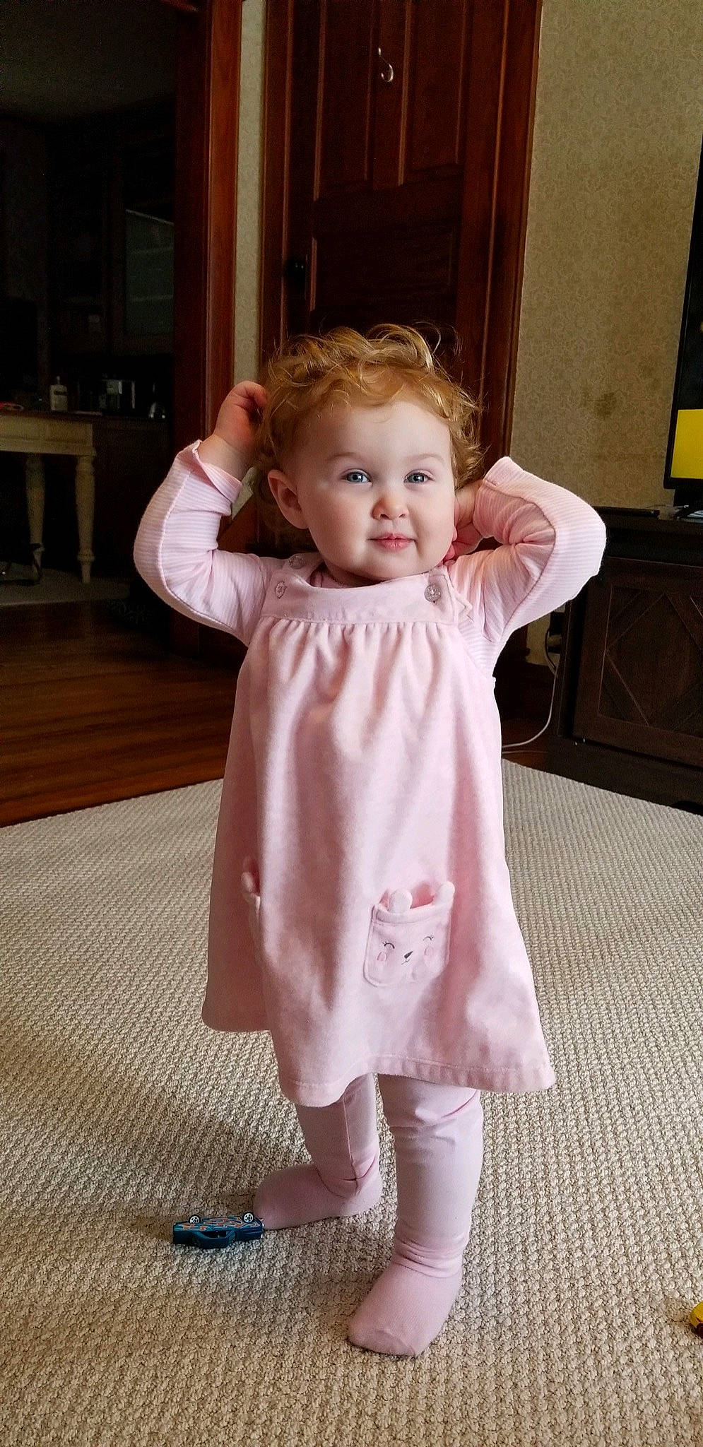 Rosalie is registered to the contest to win money with this photo: baby_toddler_clothing, cheek, dress, eye, face, floor, flooring, gesture, head, iris, joint, leg, one_piece_garment, person, pink, shoulder, skin, sleeve, smile, standing