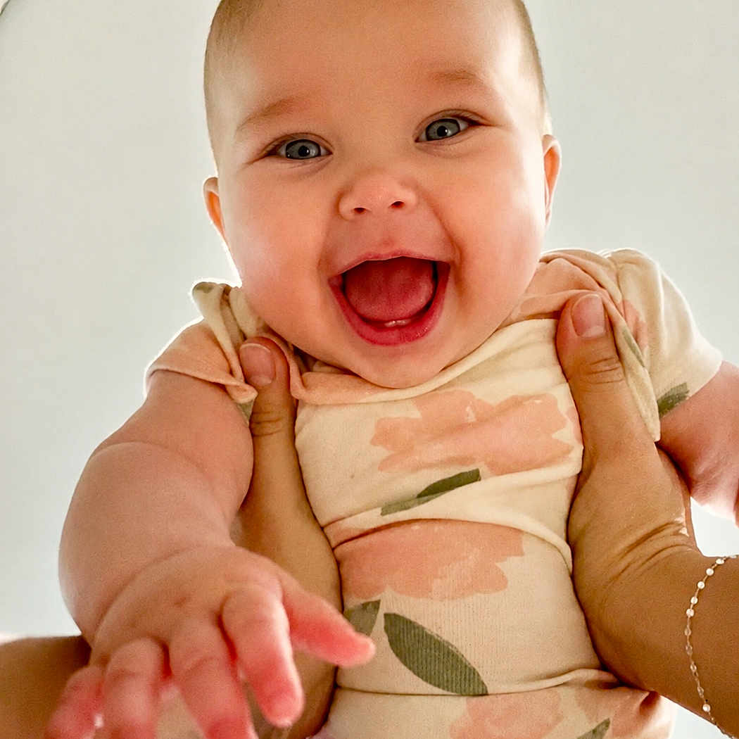Baylee is registered to the contest to win money with this photo: baby, child, smiling, happy, hands, onesie, floral, person, portrait, infant, cute, reaching, skin, face, young, joy, closeup, expression, background, casual