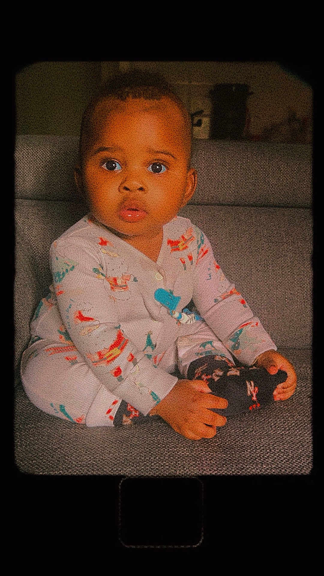 Zola a rejoint le concours — aidez-le/la à gagner de superbes lots ! baby, child, pajamas, sitting, couch, indoor, face, hands, feet, curious, wide_eyes, colorful, patterned_clothing, portrait, young_child, infant, cozy, home, soft_lighting, vintage_filter