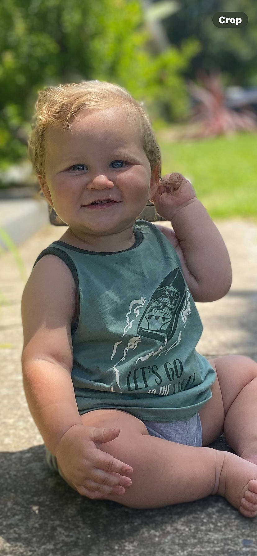 baby, casual_clothing, child, concrete, curly_hair, cute, daylight, grass, greenery, happy, nature, outdoor, playful, portrait, sitting, smiling, sunlight, tank_top, toddler, young_child