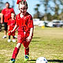 child, girl, soccer, sports, uniform, red_clothing, grass, outdoor, daylight, ball, glasses, action, team, people, field, athlete, shoelaces, socks, green_shoes, recreation