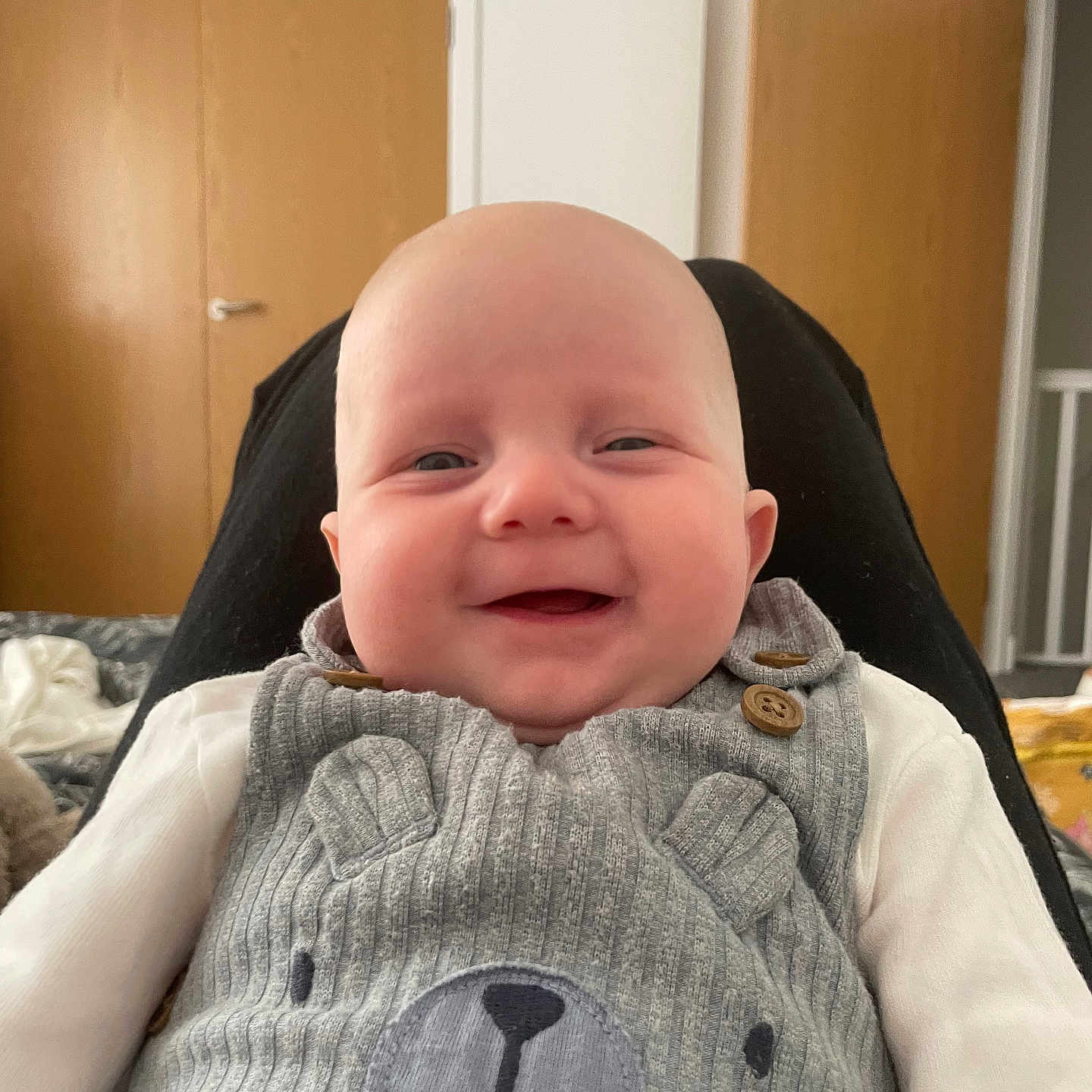 Luca joined the competition — help win amazing prizes! baby, bear_design, button, child, clothing, cozy, cute, door, face, grey_outfit, happy, indoors, infant, person, portrait, sitting, smiling, soft_lighting, white_shirt, wooden_door