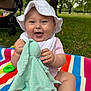 baby, child, smiling, hat, toy, blanket, bunny, outdoor, grass, park, stroller, person, cute, sitting, happy, playful, nature, greenery, bottle, sock