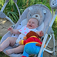Eliya joined the competition — help win amazing prizes! baby, infant, baby_rocker, plush_toy, outdoor, garden, grass, smiling, happy, child, greenery, sunlight, clothing, bib, footwear, toy, playful, person, seat, relaxing