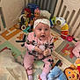 Eliya is registered to the contest to win money with this photo: baby, playpen, toy, stuffed_animal, headband, pajamas, floor_mat, child, indoor, colorful, sitting, holding, curious, soft_toy, plastic_toy, blanket, infant, cute, playtime, expression