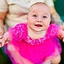 baby, child, smiling, pink_dress, blue_eyes, happy, portrait, infant, cute, person, holding_hands, outdoor, blurred_background, rosy_cheeks, toddler, clothing, face, head, joyful, closeup