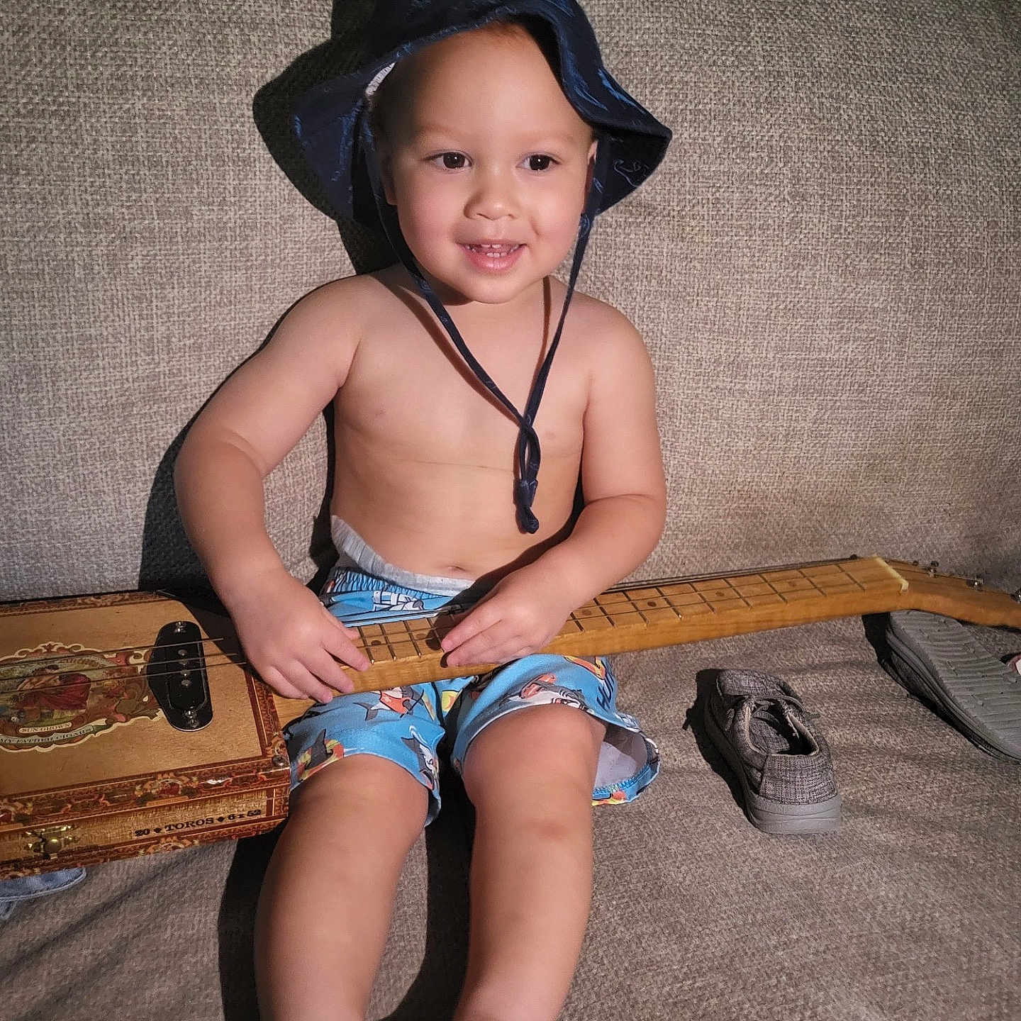 Ledger is registered to the contest to win money with this photo: baby, bodypart, bonnet, clothing, couch, face, finger, footwear, furniture, guitar, hand, hat, head, person, photography, portrait, shoe, shorts, sitting, sunhat