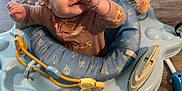Paylynn joined the competition — help win amazing prizes! baby, child, activity_jumper, blue, indoor, flooring, wooden_floor, carpet, toy, smiling, thumb_in_mouth, winking, bracelet, clothing, person, playful, home, furniture, seat, cute