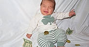 Elijah joined the competition — help win amazing prizes! baby, infant, money, dollar_bills, coins, white_blanket, clothing, sweater, striped_pants, cute, expression, sitting, indoors, currency, foot, hand, face, scrunched_face, green, cute_baby