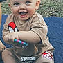 baby, child, smiling, outdoor, grass, toy, clothing, spiderman, sitting, foot, hand, quilt, happy, cute, person, infant, face, head, playful, barefoot