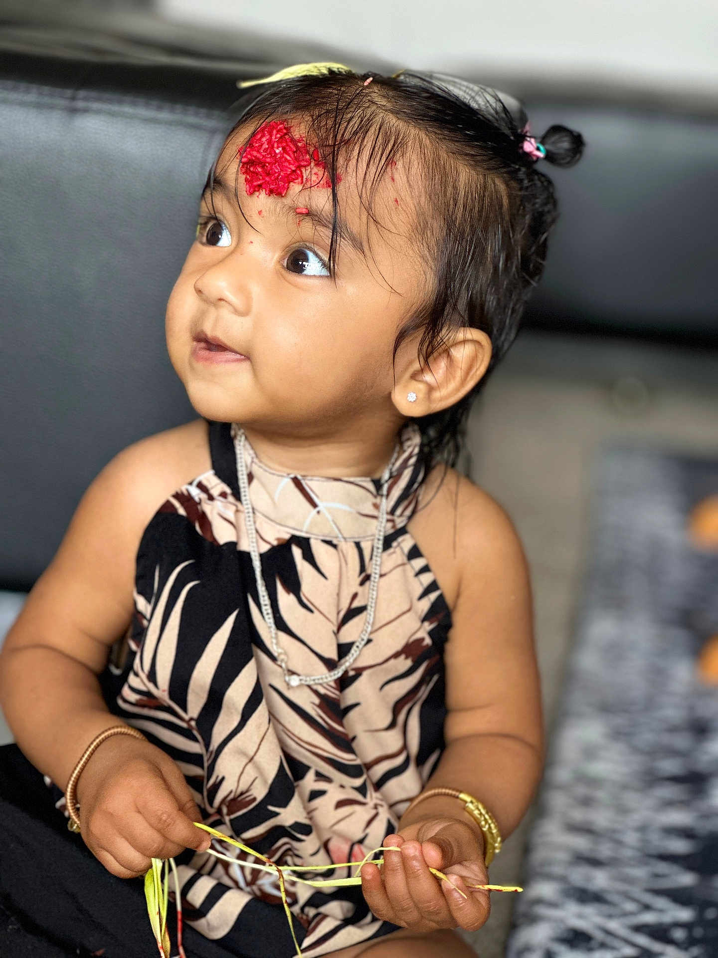 Sanbritti is registered to the contest to win money with this photo: toddler, child, girl, jewelry, bracelet, necklace, dress, patterned_clothing, face, eyes, hair, hair_tie, hand, holding, couch, indoor, decorative_mark, skin, portrait, sitting