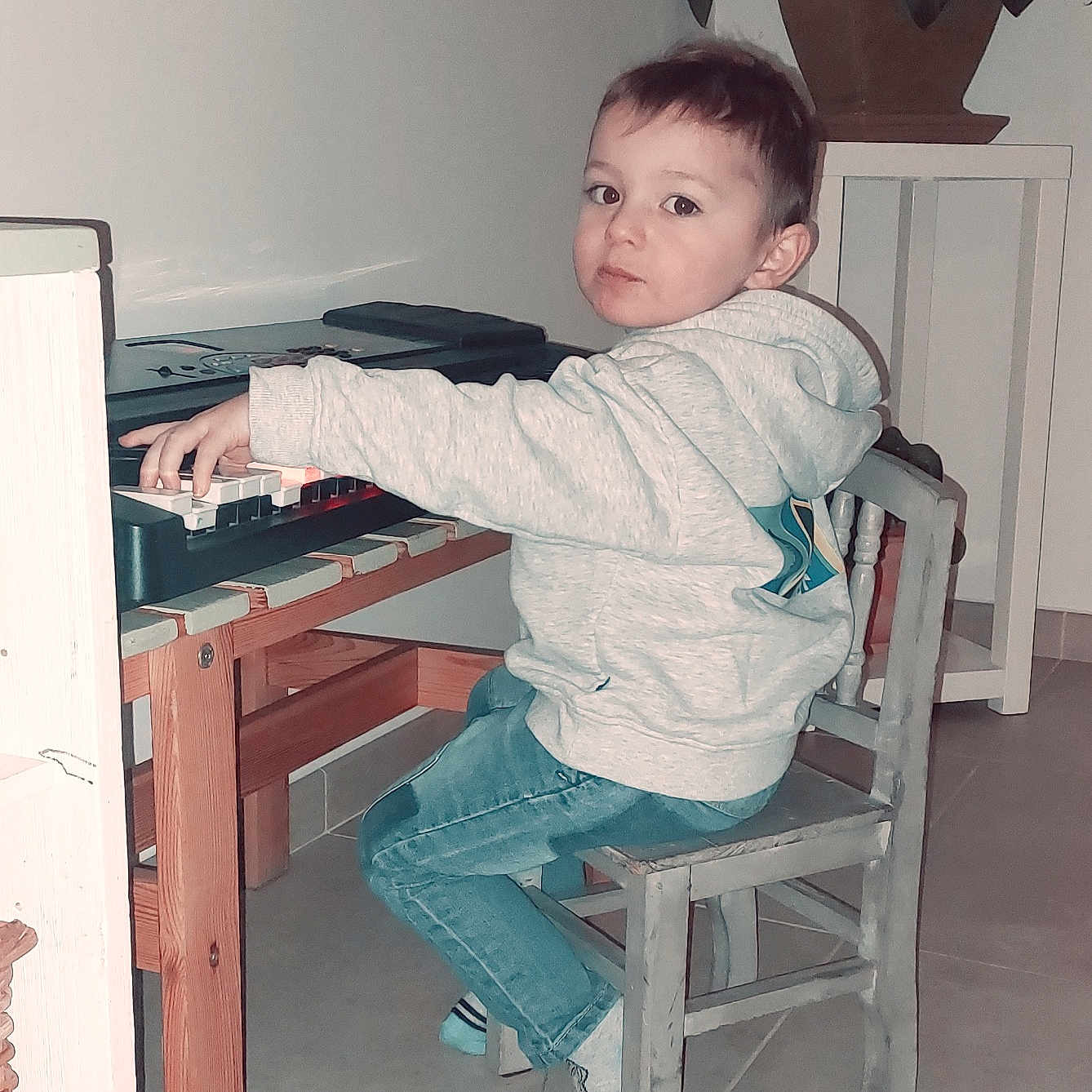 Joris participe au concours pour gagner de l'argent avec cette photo : casual_clothing, chair, child, curious_expression, floor_tiles, home, hoodie, indoor, jeans, keyboard, music, musical_instrument, person, piano, plant, playing, potted_plant, small_chair, wooden_furniture, young_child
