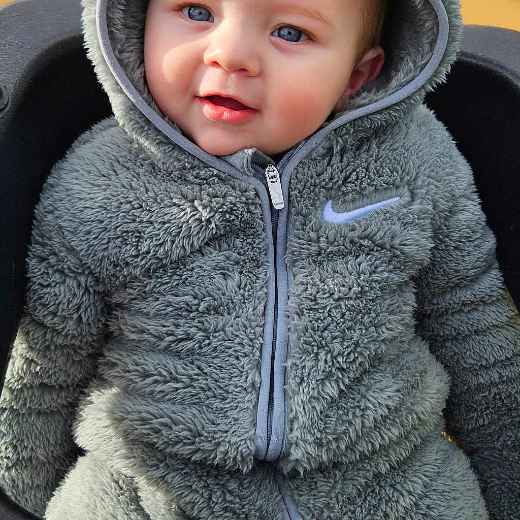 Kody is registered to the contest to win money with this photo: baby, blue_eyes, child, cozy, cute, face, gray, hoodie, infant, outdoor, person, playground, portrait, seat, smile, soft_texture, swing, warm_clothing, young_child, zipper