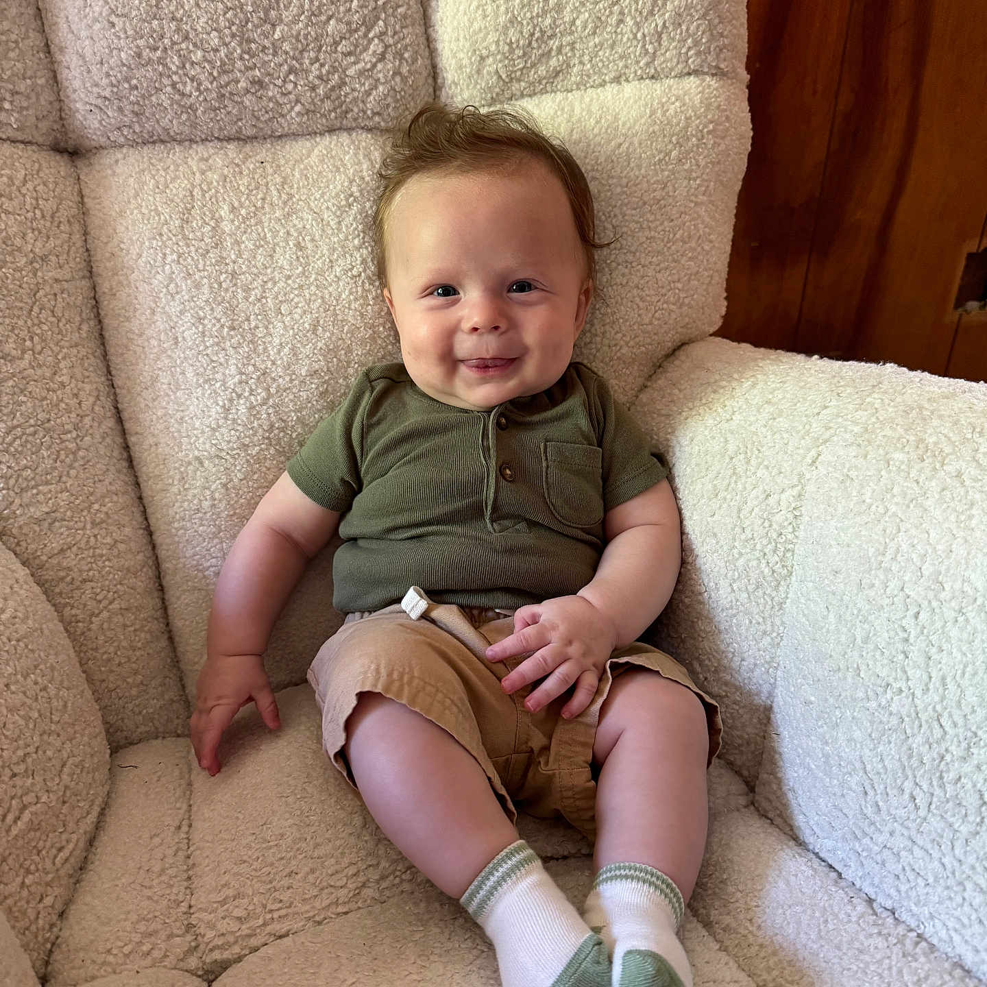 Bodie is registered to the contest to win money with this photo: armchair, baby, casual_clothing, child, comfortable, cozy, cute, fluffy_chair, furniture, green_shirt, happy, indoor, khaki_shorts, portrait, sitting, small_hands, smiling, white_socks, wood_paneling, young_child
