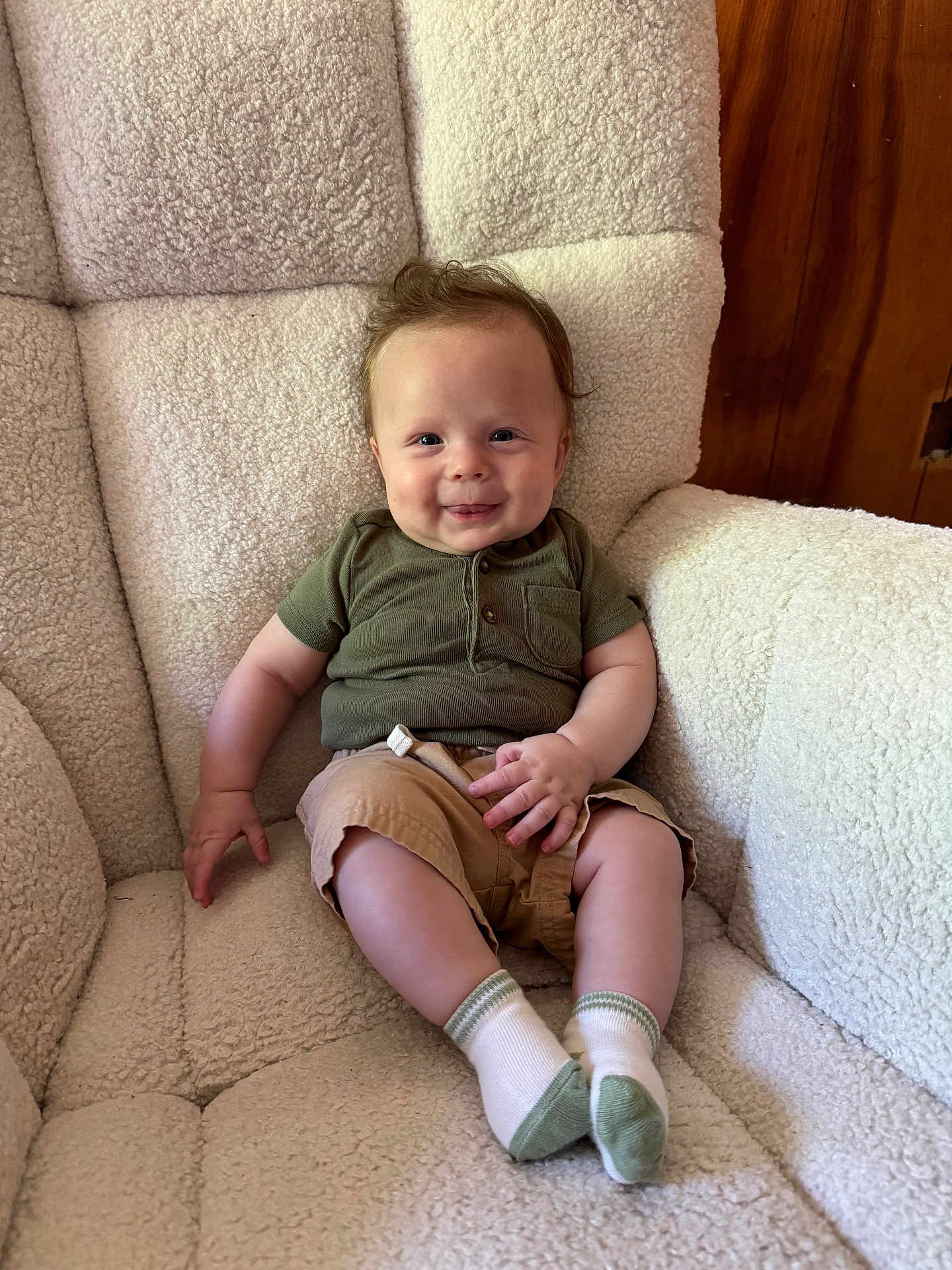 Bodie is registered to the contest to win money with this photo: baby, child, smiling, sitting, armchair, green_shirt, khaki_shorts, white_socks, indoor, cozy, fluffy_chair, cute, happy, young_child, portrait, furniture, wood_paneling, casual_clothing, small_hands, comfortable