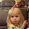 blonde_hair, boy, casual, child, children, couch, curious, flower_pattern, furniture, girl, indoor, living_room, lollipop, person, playful, portrait, red_shirt, seated, yellow_shirt, young