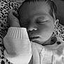 baby, sleeping, infant, cozy, knitted_sweater, patterned_cushion, black_and_white, peaceful, resting, cute, portrait, hand, face, newborn, young_child, closeup, soft_texture, indoor, comfort, relaxation