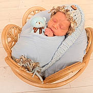 Saint is registered to the contest to win money with this photo: newborn, baby, sleeping, blue_blanket, knitted_hat, teddy_bear, wooden_basket, floor, cozy, cute, infant, portrait, child, peaceful, indoor, soft_lighting, wrapped, tiny, adorable, resting