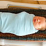 newborn, baby, swaddled, sleeping, blanket, knitted_cushion, hospital_bassinet, infant, peaceful, face, head, person, cute, resting, indoors, soft_texture, light_blue, cozy, wrapped, tiny