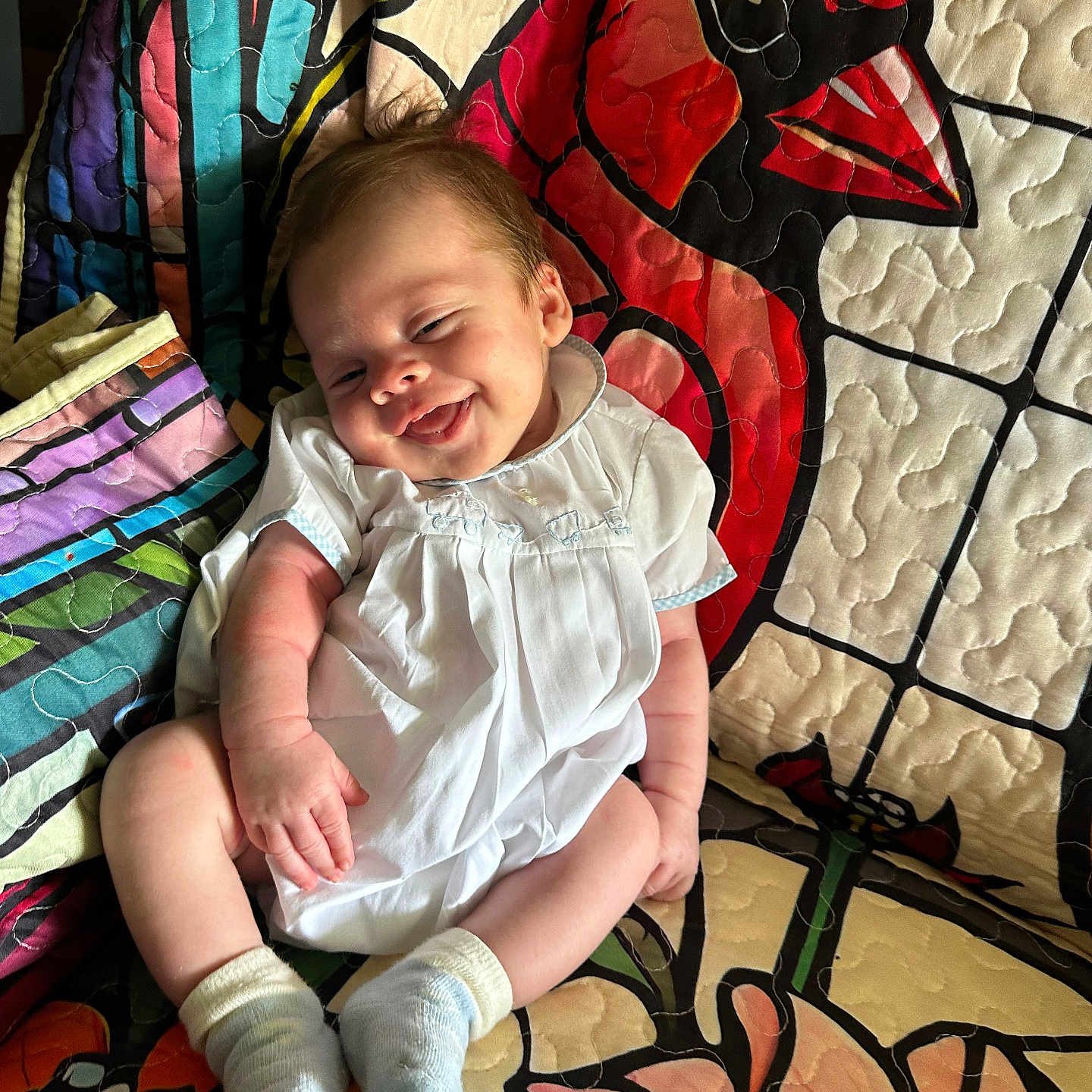 Stetson joined the competition — help win amazing prizes! baby, infant, smiling, white_clothing, sock, quilt, colorful, cardinal_bird, floral_pattern, fabric, seated, happy, cute, child, portrait, indoors, soft_light, cozy, relaxed, person