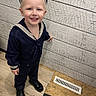 child, toddler, smiling, navy_outfit, sailor_hat, indoor, wooden_wall, floor, black_shoes, cute, portrait, standing, happy, young_child, fashion, clothing, person, blond_hair, face, blue_eyes