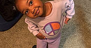 Nyomi is registered to the contest to win money with this photo: backpack, bed, blanket, carpet, casual, child, cute, earrings, floor, girl, hair_buns, indoor, nike_slides, person, playful, portrait, purple_clothing, room, smiling, toy