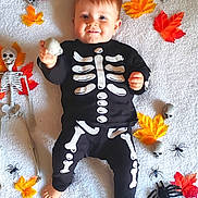 Amaël a rejoint le concours — aidez-le/la à gagner de superbes lots ! autumn_leaves, baby, child, costume, cute, decorations, festive, halloween, happy, holiday, indoors, lying_down, plastic_spider, playful, seasonal, skeleton_costume, skeleton_prop, skull, smiling, white_blanket