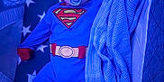 Archie is registered to the contest to win money with this photo: baby, bassinet, blanket, blue, child, comfort, crib, cute, face, indoor, infant, knitted_blanket, onesie, pacifier, red, rest, sleeping_area, soft_lighting, star_pattern, superman_costume