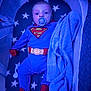 baby, superman_costume, pacifier, blanket, crib, bassinet, star_pattern, blue, red, onesie, child, infant, sleeping_area, knitted_blanket, cute, soft_lighting, indoor, comfort, rest, face