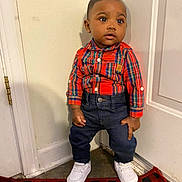 Tylan is registered to the contest to win money with this photo: toddler, child, standing, red_shirt, plaid, jeans, white_sneakers, indoor, door, wall, curious, young_child, fashion, casual_wear, floor, rug, small_person, portrait, cute, person
