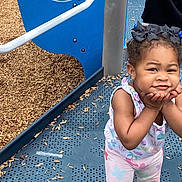Ariel joined the competition — help win amazing prizes! blue, child, clothing, cute, daylight, face, hair_bows, hand_on_face, legs, outdoor, patterned_pants, person, playground, playground_equipment, purple, smiling, standing, toddler, white, wood_chips
