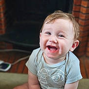 Charly a rejoint le concours — aidez-le/la à gagner de superbes lots ! baby, background_blur, brick, cartoon, child, cute, face, fireplace, happy, indoor, infant, joyful, light_blue, person, portrait, shirt, sitting, smiling, toddler, young_child