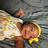Kaiomi joined the competition — help win amazing prizes! baby, infant, child, portrait, lying_down, bed, bedding, gray_background, yellow_headband, floral_clothing, dress, face, eyes, looking_at_camera, indoor, home, relaxed, sleeping_area, close_up, photography