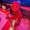 baby, child, infant, smiling, face, portrait, indoor, bedroom, bed, blanket, toy, activity_center, playtime, seated, standing, colorful_lighting, red_light, blue_light, happy, home