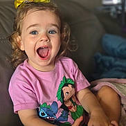 Joy participe au concours pour gagner de l'argent avec cette photo : toddler, child, smiling, curly_hair, yellow_bow, pink_shirt, animated_characters, sitting, couch, blanket, happy, indoors, playful, portrait, young_child, blue_eyes, casual_clothing, expression, cute, fun