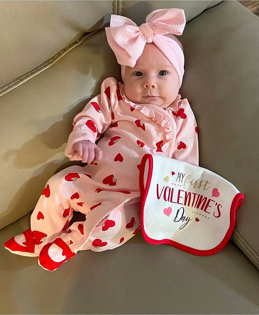 Jemma is registered to the contest to win money with this photo: baby, baby_products, baby_toddler_clothing, carmine, child, collar, comfort, dress, fashion_accessory, font, happy, headwear, linens, outerwear, pattern, person, pink, room, sitting, sleeve