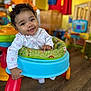 baby, child, walker, smiling, curly_hair, indoor, playroom, toys, colorful, happy, person, infant, clothing, floor, furniture, seat, cute, young, portrait, hand