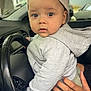 toddler, child, baby, cap, hoodie, hand, steering_wheel, car_interior, curious, portrait, clothing, seat, driving, vehicle, window, urban, casual, person, cute, indoor