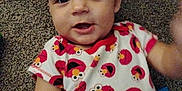 Hudson is registered to the contest to win money with this photo: baby, infant, onesie, elmo, carpet, child, smiling, face, cute, playful, clothing, lying_down, hand, eyes, expression, indoors, person, toddler, pattern, red