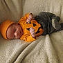 Micha is registered to the contest to win money with this photo: baby, infant, orange_hat, orange_shirt, pumpkin_face, striped_socks, gray_pants, blanket, lying_down, cute, smiling, indoors, cozy, child, newborn, celebration, holiday_outfit, soft_texture, portrait, resting