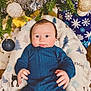 baby, infant, blue_clothing, blanket, christmas_tree, christmas_ornaments, holiday, decorations, face, eyes, hands, indoor, festive, cute, child, smiling, seasonal, cozy, portrait, celebration