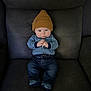 Colt is registered to the contest to win money with this photo: baby, child, infant, hat, knit_hat, blue_clothing, jeans, socks, sitting, leather_couch, indoor, portrait, cute, hands_clasped, serious_expression, person, young_child, cozy, casual_clothing, home