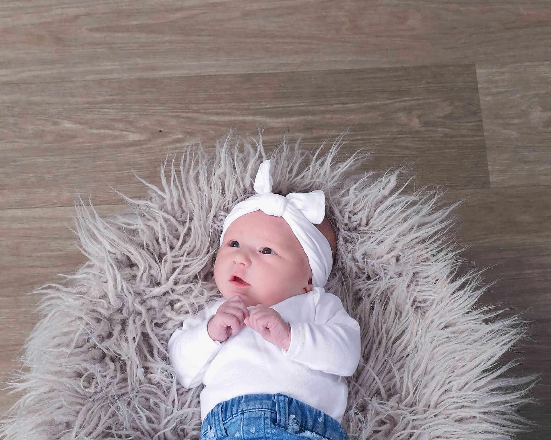 Everly is registered to the contest to win money with this photo: baby, infant, headband, white_clothing, blue_jeans, fluffy_rug, wooden_floor, cute, newborn, portrait, lying_down, indoor, soft_texture, small_hands, curious_look, child, adorable, fashion, clothing, casual