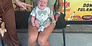 Kayson joined the competition — help win amazing prizes! baby, woman, smile, pointing, green_clothing, bow_tie, chair, outdoor, concrete_floor, sandals, tattoo, sign, text, celebration, happy, people, casual, portrait, friendship, fun