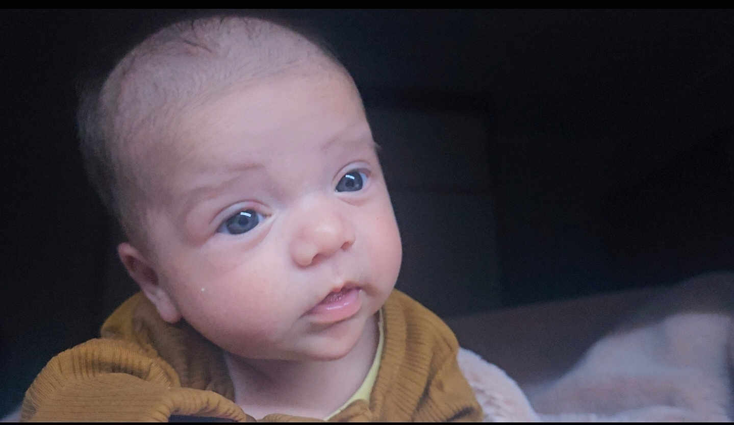 Ellie is registered to the contest to win money with this photo: baby, infant, face, blue_eyes, curious, close_up, portrait, child, young, cozy, clothing, indoors, soft_light, expression, skin, head, person, cute, warm, baby_clothes